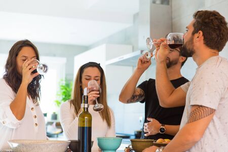 Smiling young friends tasting wine. Group of cheerful people standing near table and drinking wine. Wine tasting conceptの写真素材