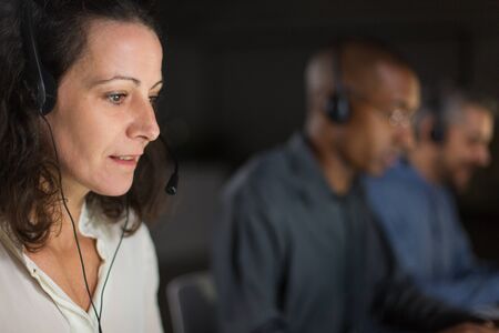 Cheerful mature call center operator looking at laptop screen. Smiling curly woman working in...