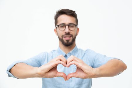 Cheerful young man showing hand heart gesture. Handsome happy young man showing hand heart symbol and smiling at camera. Love conceptの写真素材