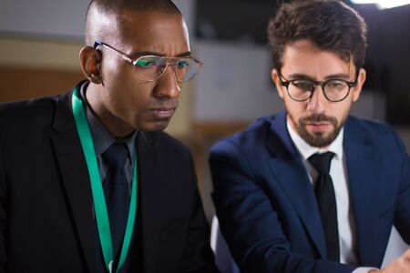Two focused managers looking at laptop screen. Concentrated office managers working together over new project. Teamwork, working late conceptの写真素材