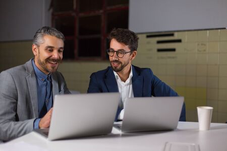 Content businessmen discussing work in dark office. Cheerful professional business colleagues using laptop computers and working late at night. Cooperation conceptの写真素材