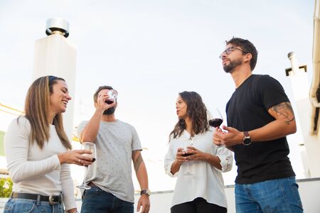 Low angle shot of smiling people drinking red wine and talking. Cheerful friends holding glasses...
