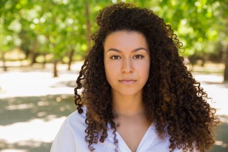 Beautiful curly woman standing and looking at camera. Attractive young lady with long hair posing in...