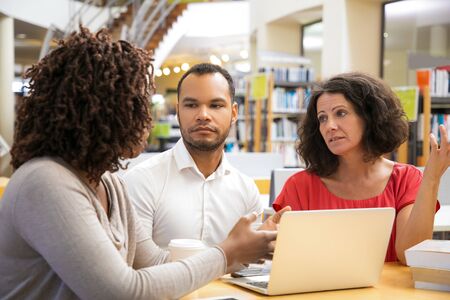 Thoughtful people working at library. Focused students studying with laptop at library. Education,...