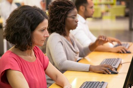 Focused students working with computers at library. Thoughtful young people searching information...