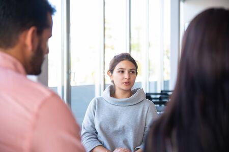 Focused young psychologist talking to workers. Group of young people listening young woman. Training...