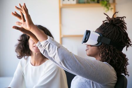 Side view of excited woman testing VR headset. Cheerful African American woman wearing virtual...