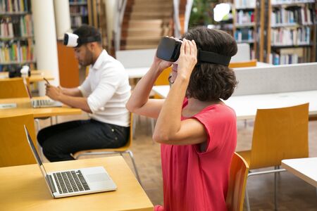 Curly mature woman wearing VR headset. Confident mature user holding virtual reality glasses while...