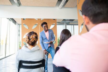 Smiling consultant communicating with young workers. Handsome cheerful African American man talking...