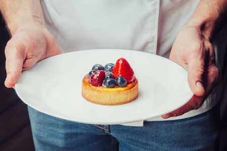 Restaurant chef holding plate with sweet dessert. Close-up of unrecognizable male cook showing refreshing dessert. Bakery cafe conceptの写真素材