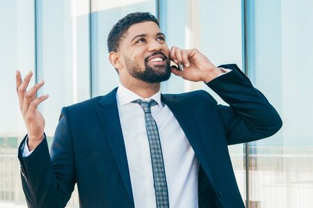 Cheerful businessman talking on phone and celebrating good news and success. Young Latin man in...