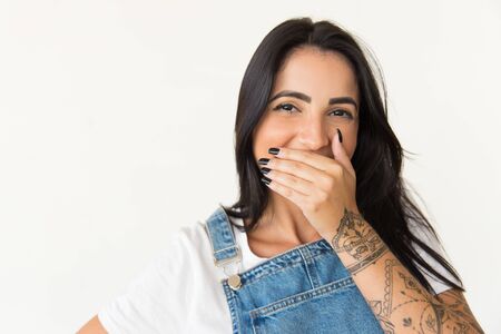Cheerful woman laughing and looking at camera. Portrait of content young brunette woman closing mouth with hand isolated on white background. Positive emotion conceptの写真素材