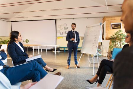Confident business consultant working with employees. Group of cheerful workers sitting on chairs and listening speaker. Business meeting conceptの写真素材
