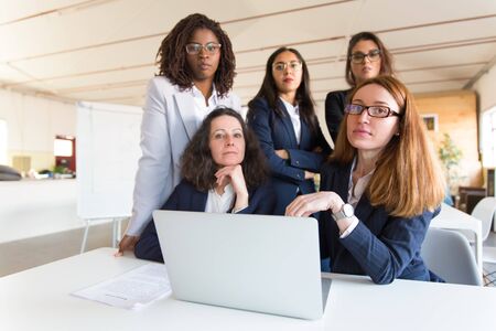Group of confident businesswomen looking at camera. Professional office managers posing near table...