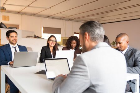 Smiling business people working with laptops in office. Group of cheerful managers sitting at table...