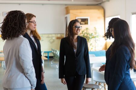 Group of smiling female managers talking in open space office. Cheerful young women standing in...