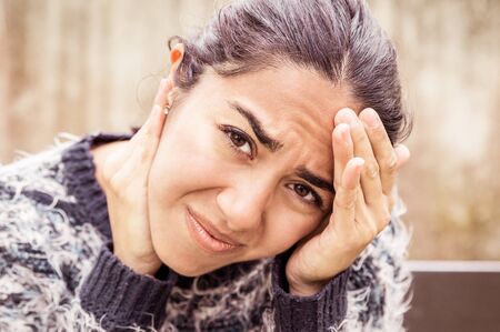 Tensed pretty woman touching head outdoors. Young lady wearing sweater, looking at camera and...