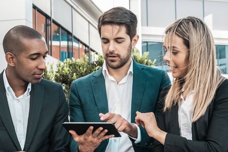 Marketing team analyzing report on tablet screen. Business people meeting outdoors, using digital device together and staring at screen with interest. Collaborating on project conceptの写真素材