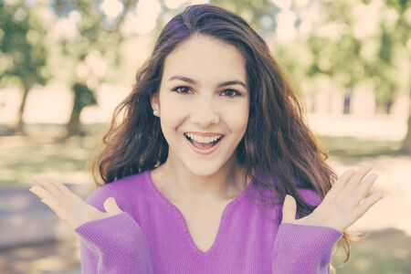 Happy pretty young woman throwing up hands in park. Beautiful lady wearing sweater and looking at...
