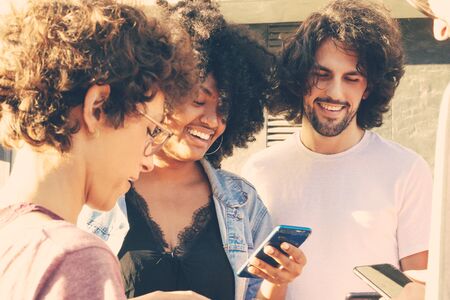 Interracial team of friends standing in circle and using smartphones. Users holding mobile phones...
