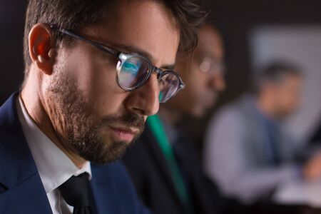 Focused handsome businessman sitting and working with laptop. Side view of focused man in eyeglasses...