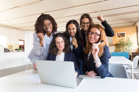Group of successful businesswomen with raised fists with laptop. Professional office managers posing near table with laptop. Business success, teamwork conceptの写真素材