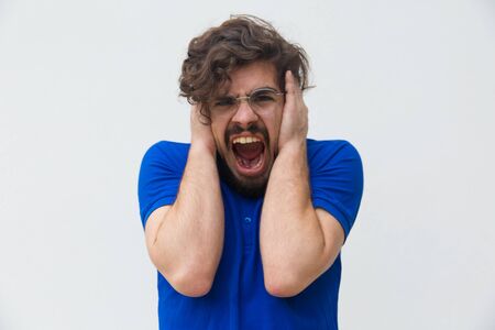 Front view of angry young man screaming. Angry man screaming loud with wide open mouth and holding...