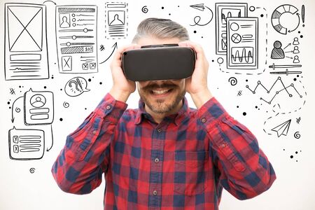 Hand drawn UI or UX pictures with excited guy holding VR headset. Studio shot of young man testing...