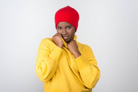 Beautiful cheerful African American woman looking at camera. Attractive young lady wearing yellow turtleneck sweater and red hat. Female beauty conceptの写真素材