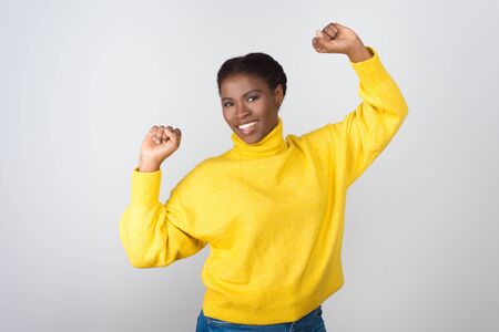 Happy young woman celebrating success. Beautiful cheerful young African American woman raising fists and smiling at camera. Winner conceptの写真素材