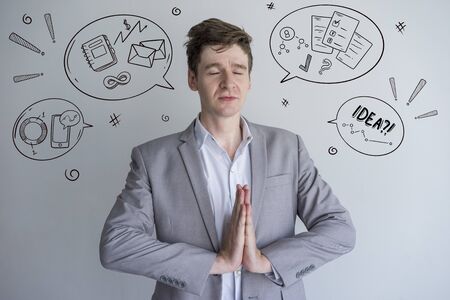 Calm male manager meditating with hand drawn business sketches. Man making Namaste gesture. Peaceful...