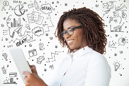 Smiling young businesswoman with tablet pc and hand drawn business doodles around her. Low angle...