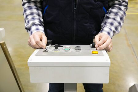 Cropped shot of factory machine operator pressing buttons at control panel. Hands of man working in vest and checkered shirt working at plant. Technology or production process conceptの写真素材