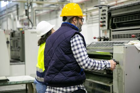 Two factory employees working with printing machine. Professional operators working at printing house. Print manufacturing conceptの写真素材