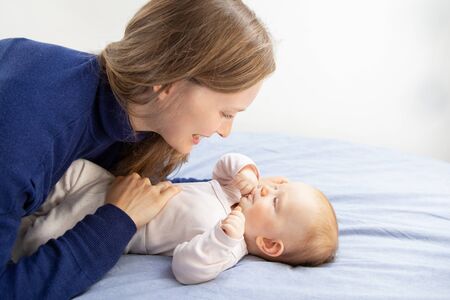 Happy mother looking at cute baby. Cheerful young mother looking at adorable baby daughter lying on...