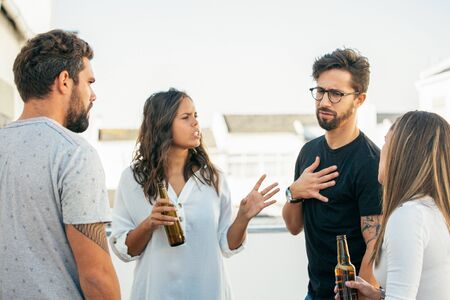 Group of friends drinking beer, talking and arguing on outdoor terrace. Young men and women in...
