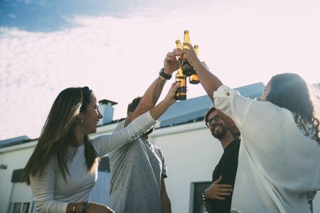 Team of happy friends celebrating success and toasting beer on outdoor terrace. Young men and women in casual meeting outside. Party or toast conceptの写真素材