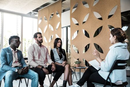 Diverse team of colleagues consulting coach. Group of young men and women sitting in training room, talking, discussing work issues . Business coaching conceptの写真素材