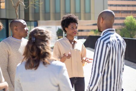 Group of young friends standing on street and communicating. Smiling African American woman talking to friends. Communication conceptの写真素材