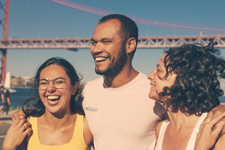 Cheerful friends embracing outdoors. Group of happy multiethnic friends walking together and laughing at riverside. Friendship conceptの写真素材