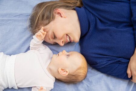 Mother and child lying on bed. Top view of happy young mother and adorable infant daughter lying...