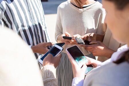 Cropped view of young people using smartphones. Closeup view of friends standing in circle on street...