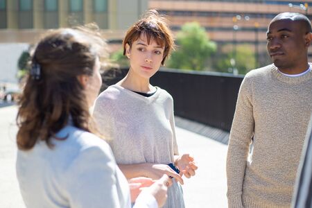 Group of serious people standing on street and talking. Concentrated friends discussing some...