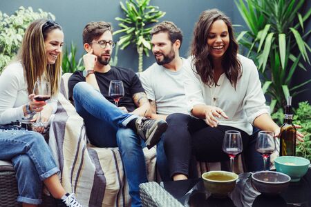 Two happy couples drinking wine and relaxing on outdoor terrace. Young men and women in casual...