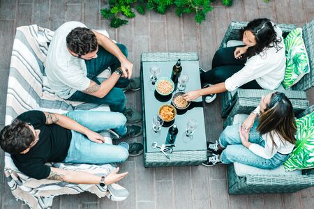 High angle of four friends sitting together on terrace, drinking wine, eating snacks and chatting. Young men and women in casual meeting outside. Wine with friends conceptの写真素材