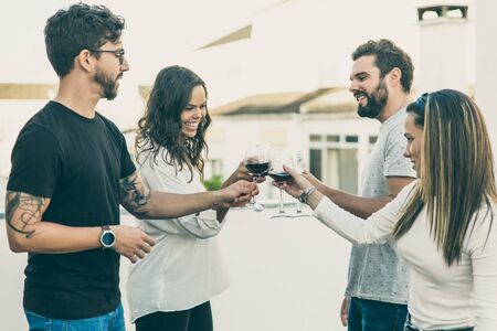 Happy people toasting wine and celebrating event on apartment balcony. Young men and women in casual...