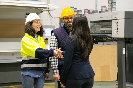 Smiling factory worker shaking hands with office manager. Cheerful employees communicating at...