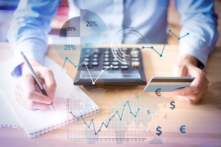 Woman holding credit card with financial analysis graphs. Cropped view of person making notes and...