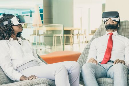 Young business people in virtual reality headsets. Focused young African American businessman and businesswoman sitting and using VR headsets in office. Business and technology conceptの写真素材