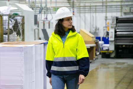 Serious female industrial professional watching production process in workshop. Middle aged woman in...